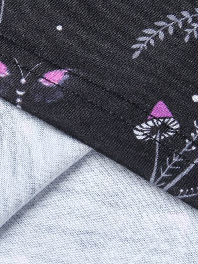 Close view of the stitched mini-dress hem on black fabric printed with purple flowers and tiny mushroom shapes.