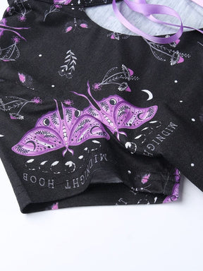 Purple moths with detailed wing markings printed on the black dress beside crescent moons, tiny mushrooms and leafy stems. Small curved lettering surrounds the moth artwork.