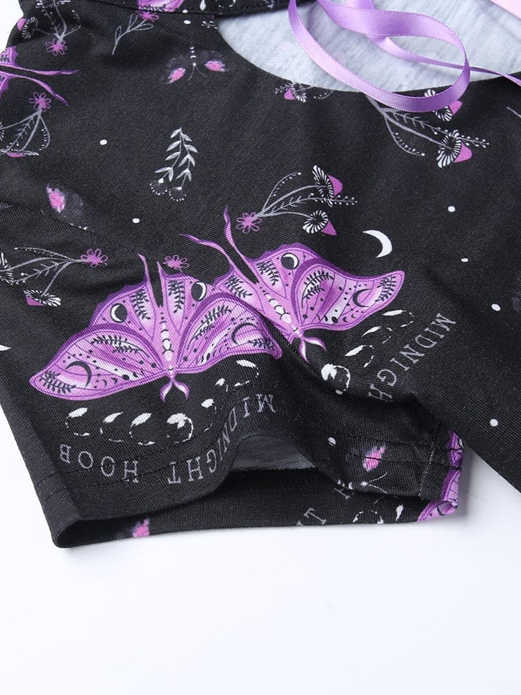 Purple moths with detailed wing markings printed on the black dress beside crescent moons, tiny mushrooms and leafy stems. Small curved lettering surrounds the moth artwork.