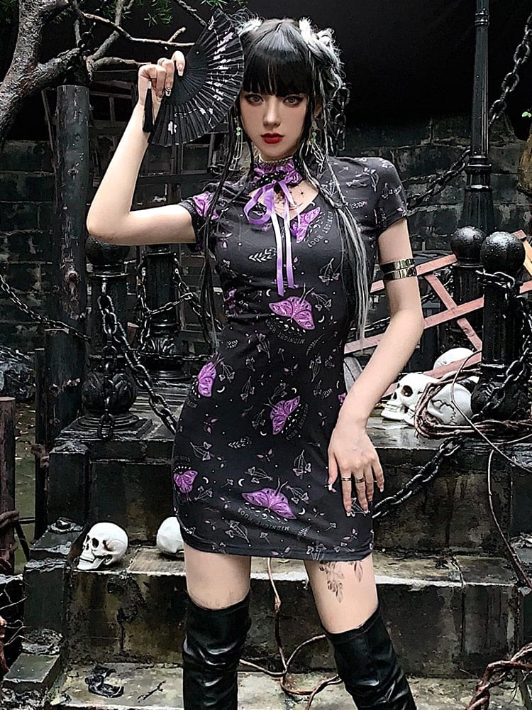 Full view of the purple moth cheongsam-inspired dress styled with tall black boots and a folding fan. The short sleeves and close-cut mini shape are visible.
