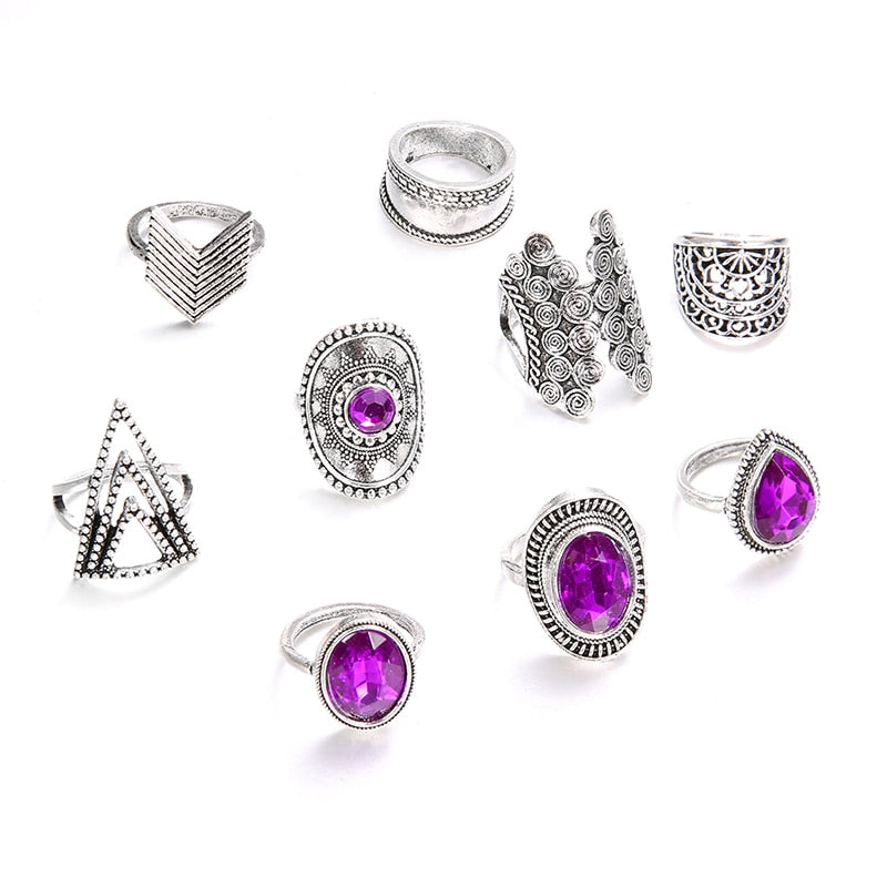 Nine-piece silver-tone ring set with purple jewel-like accents displayed together on white.