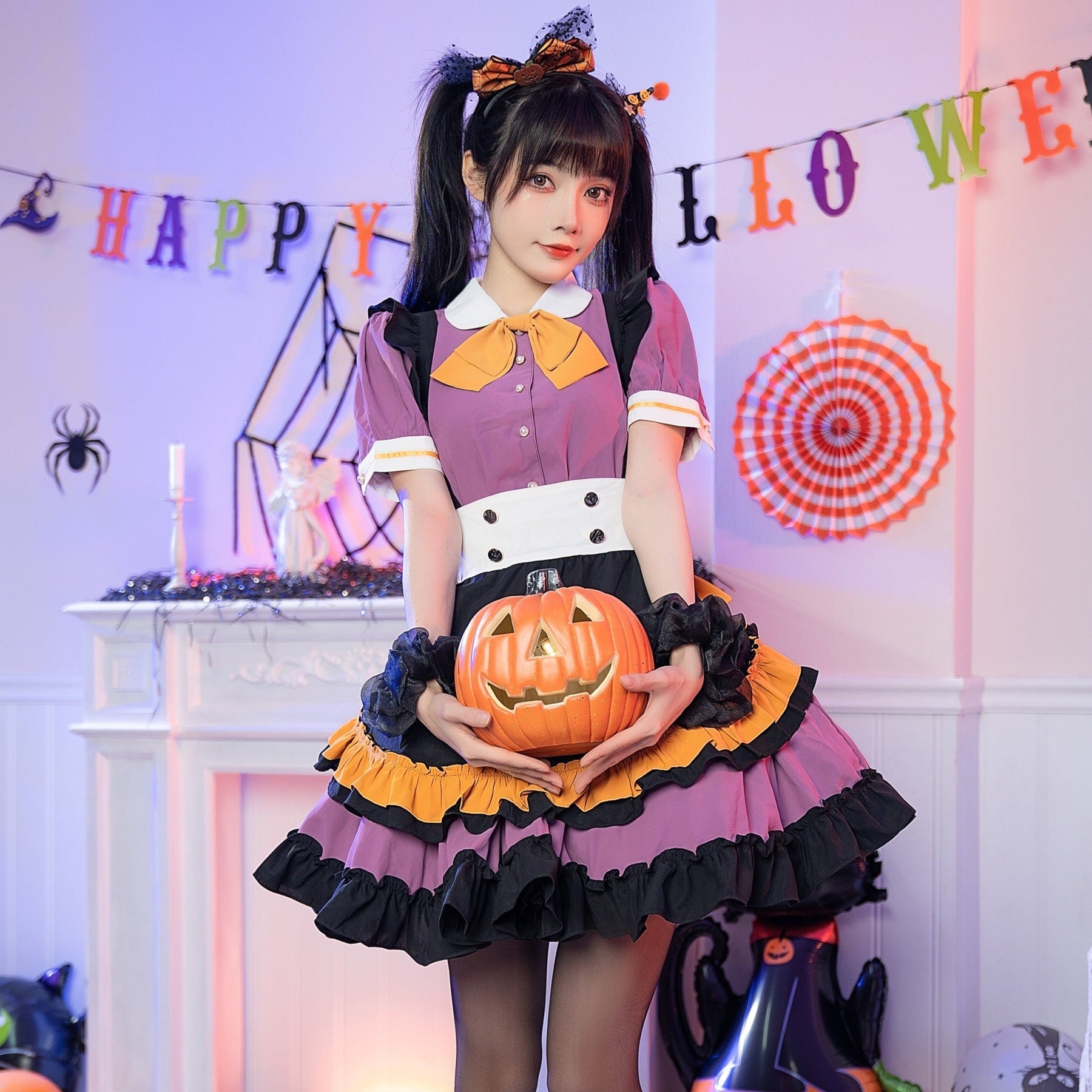 Model holding a pumpkin bucket at the waist of the purple Halloween dress, showing the orange bow, black shoulder ruffles and layered skirt.