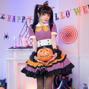 Model holding a pumpkin bucket at the waist of the purple Halloween dress, showing the orange bow, black shoulder ruffles and layered skirt.