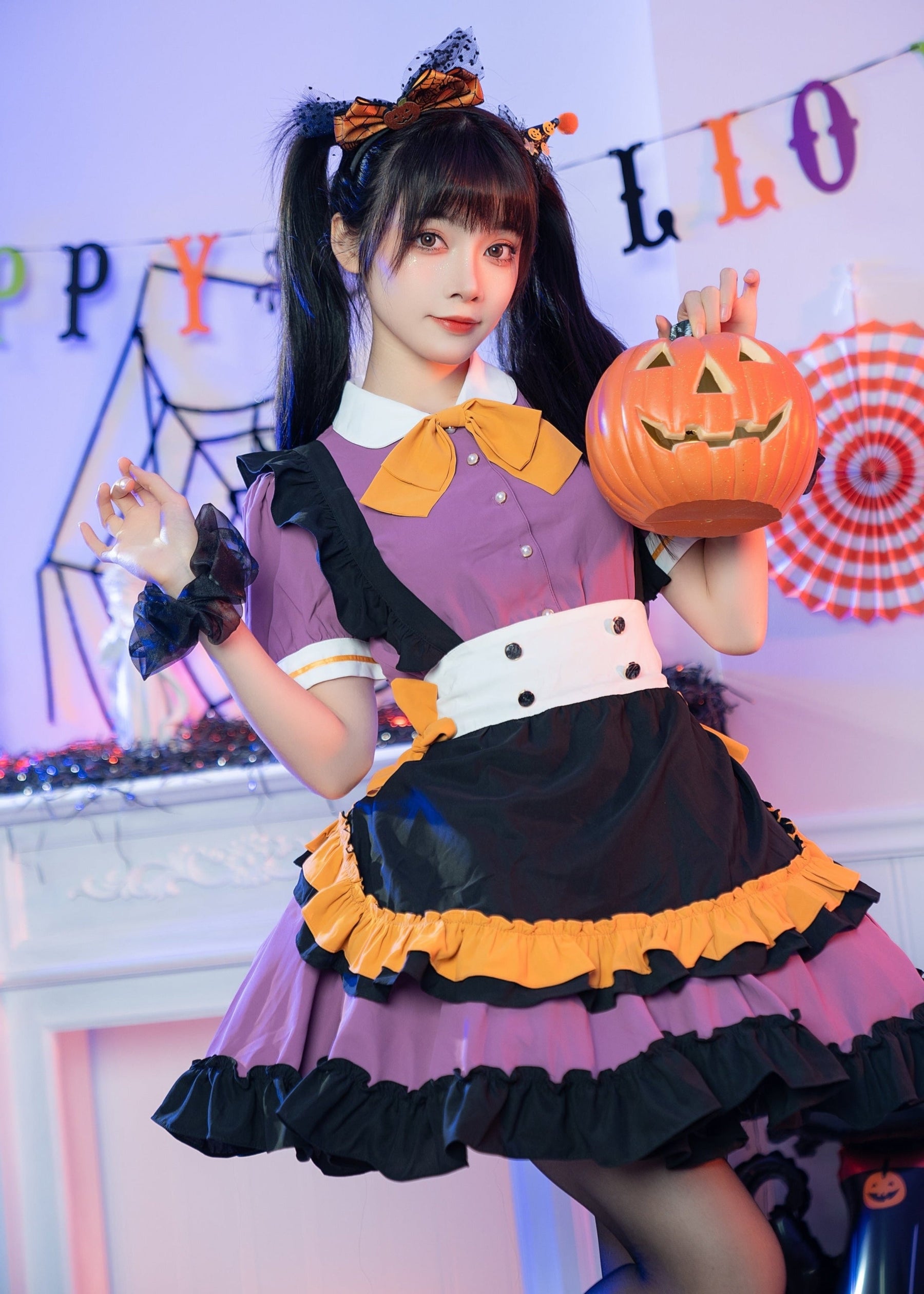 Purple and black Halloween dress worn with a pumpkin bucket raised to one side. The orange-trimmed apron panel and short puff sleeves are visible.