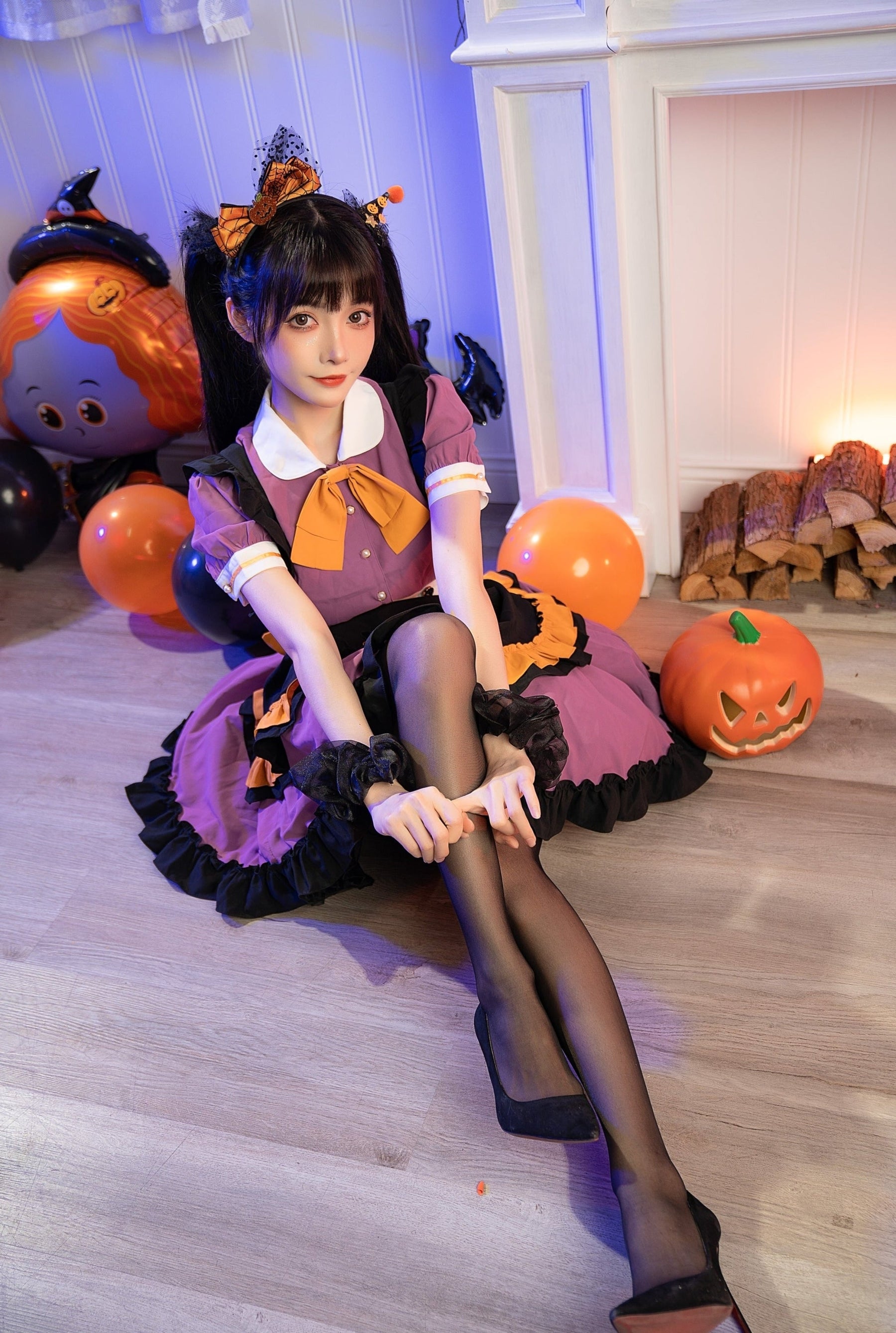 Seated full-outfit view of the purple ruffle dress with black tights and heels, surrounded by orange and black Halloween balloons.