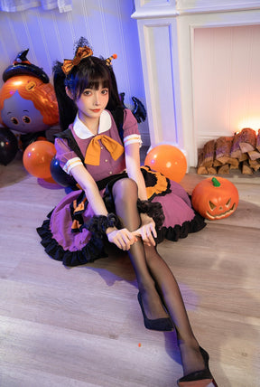 Seated full-outfit view of the purple ruffle dress with black tights and heels, surrounded by orange and black Halloween balloons.