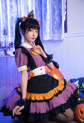 Kneeling model wearing the Pumpkin Queen dress, showing the white waistband, orange bow and black apron front against a decorated fireplace.