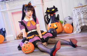 Wide seated view of the purple Halloween dress with the layered skirt spread around the model and a pumpkin bucket beside the knees.