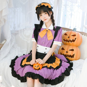 Purple ruffle dress worn while seated against white curtains with stacked pumpkin props, making the black apron and orange edging stand out.