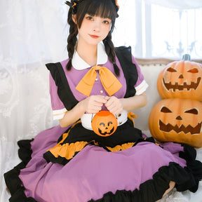 Seated close view of the purple Halloween dress with a small pumpkin prop, showing the white waistband and black-trimmed skirt tiers.