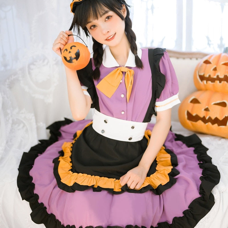 Front detail of the Pumpkin Queen dress on a seated model holding a small orange pumpkin prop beside the face, with the collar bow and ruffles visible.