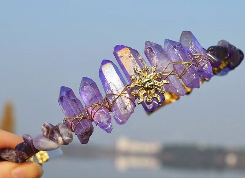 Purple crystal point tiara with a gold-tone sun face, ornate radiating rays and wire wrapping along the band.