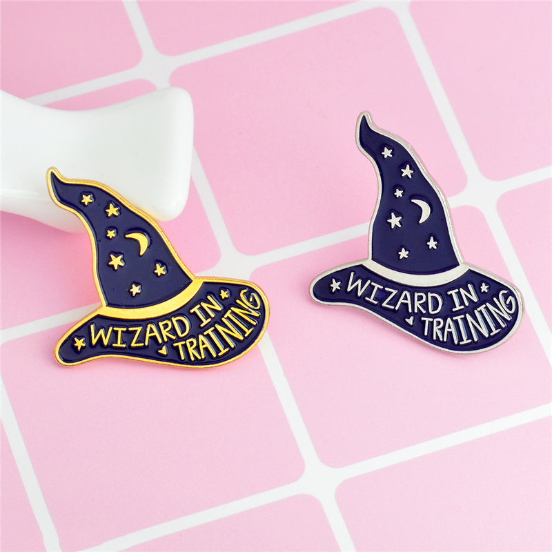 Two purple Wizard in Training hat pins on pink, comparing gold-tone and silver-tone details.