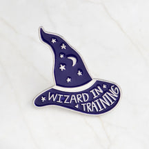 Purple Wizard in Training enamel pin with silver-tone lettering, a crescent moon and scattered stars.