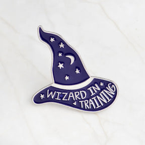 Purple Wizard in Training enamel pin with silver-tone lettering, a crescent moon and scattered stars.