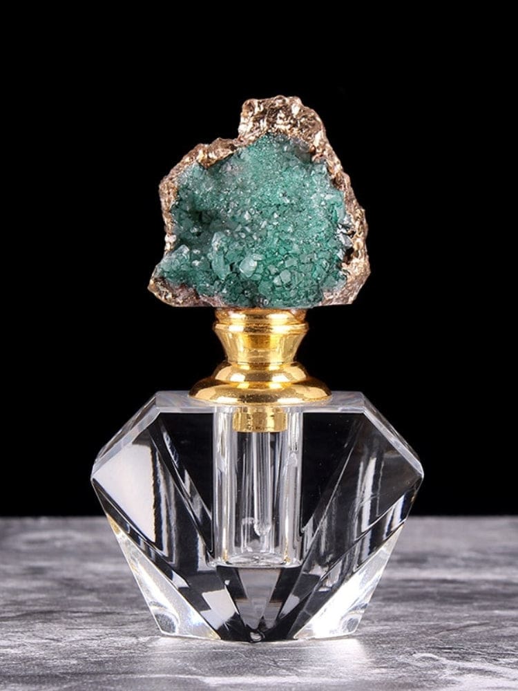 Green quartz-topped perfume bottle with a clear faceted base, gold-tone neck and irregular crystal cluster outlined by metallic edging.