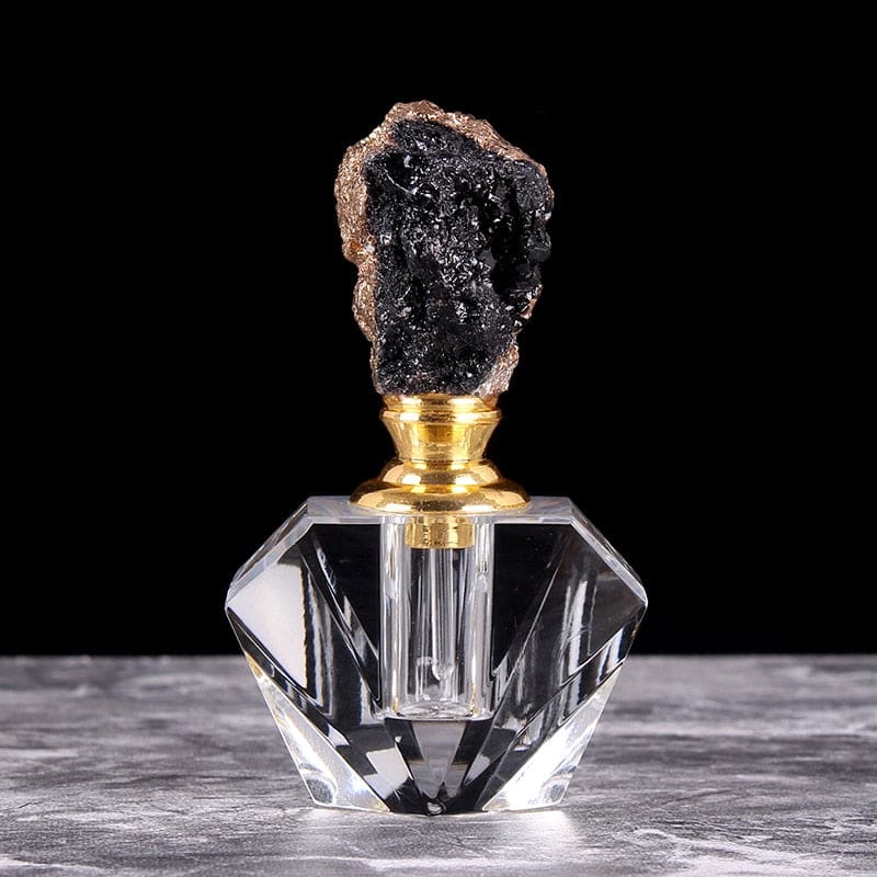Black crystal cluster stopper with metallic-tone edging on a clear faceted perfume bottle, displayed on a pale textured surface.