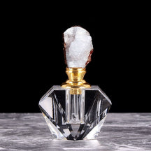 White crystal cluster stopper on a small clear perfume bottle, with warm metallic-tone details around the neck and crystal edge.