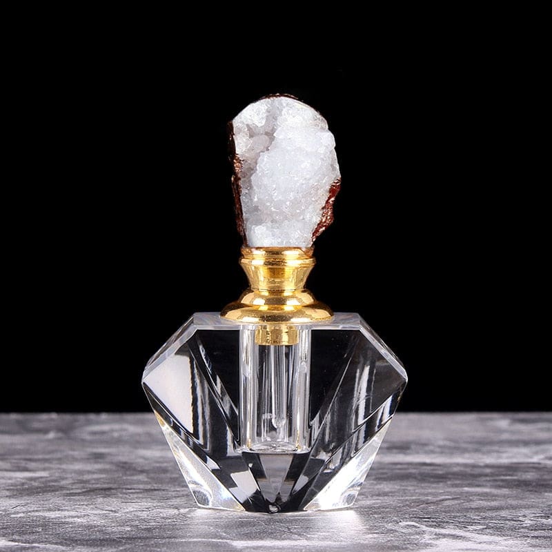 White crystal cluster stopper on a small clear perfume bottle, with warm metallic-tone details around the neck and crystal edge.
