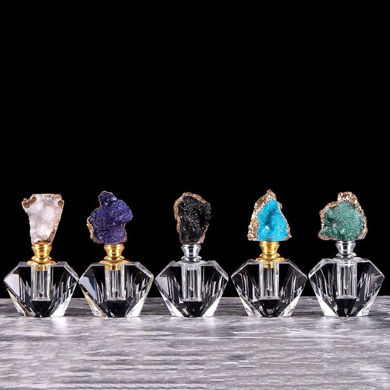 Five decorative perfume bottles with white, purple, black, blue and green crystal-topped stoppers lined up against a dark background.
