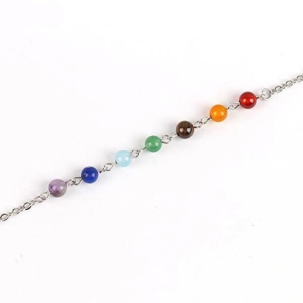Rainbow chakra bracelet laid diagonally, showing purple, blue, green, brown, orange and red beads between fine chain links.