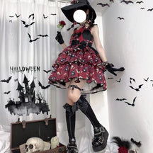Red tiered Halloween bow dress worn indoors with a black pointed hat and dark footwear, showing the full printed skirt against bat decorations.