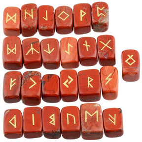 Red jasper rune stone set laid out in rows, showing individual gold-coloured characters and one unmarked stone against brick red with darker markings surfaces.
