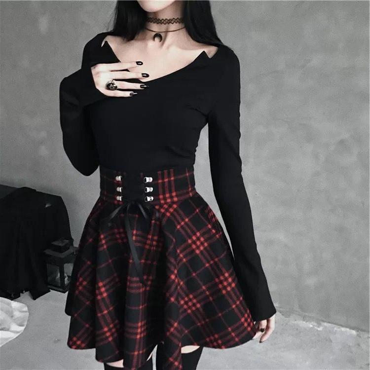 Red and black plaid mini skirt with a wide ribbon-laced waistband, worn with a black top against a gray wall.