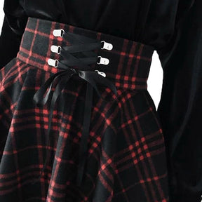 Close view of the red plaid waistband with black ribbon crossed through silver-tone loops and tied at the front.