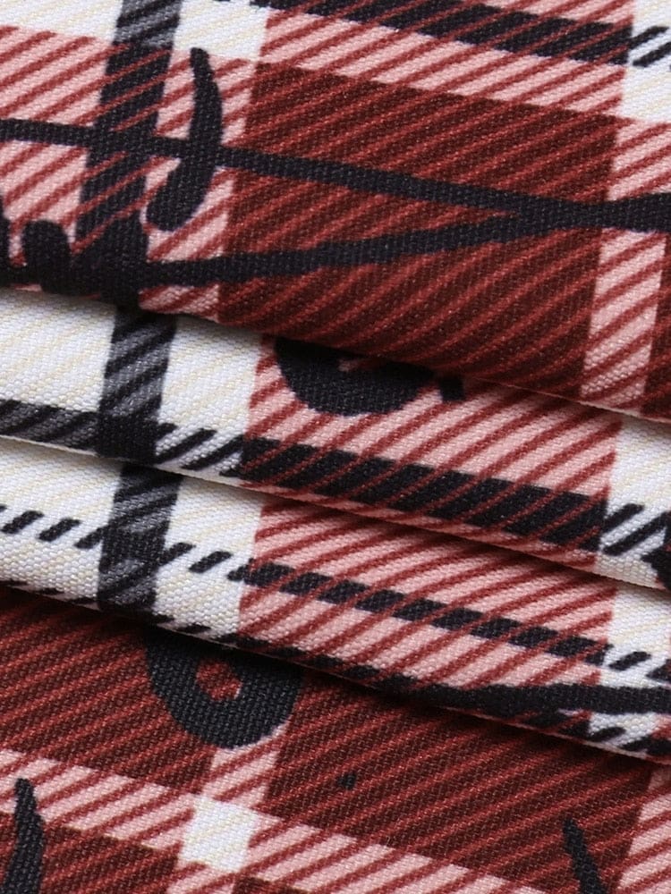 Macro view of folds in the red tartan fabric, showing fine diagonal lines in the checks and parts of the black safety-pin motif.