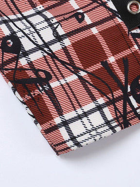 Detailed view of red, black and white plaid fabric printed with small skulls and large safety-pin outlines. A black eyelet band crosses the upper corner.