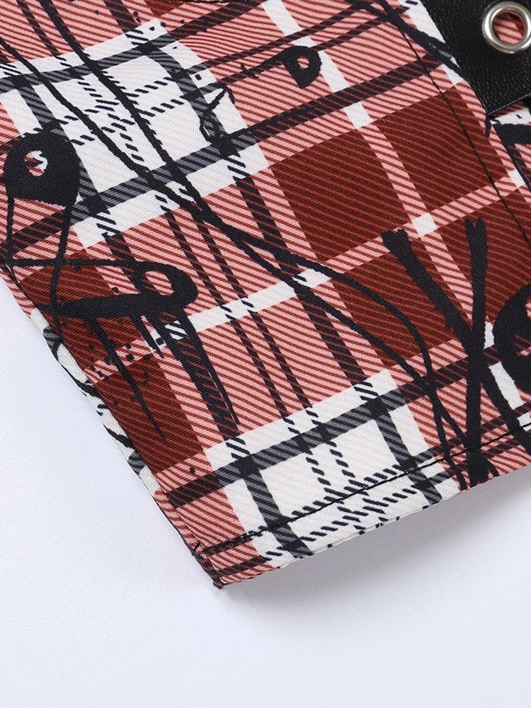 Detailed view of red, black and white plaid fabric printed with small skulls and large safety-pin outlines. A black eyelet band crosses the upper corner.