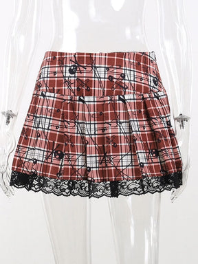 Red tartan plaid pleated mini skirt on a clear mannequin, with small black skull and safety-pin motifs and a scalloped floral lace hem.