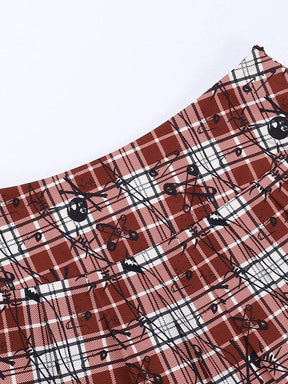 Close-up of the red plaid skirt waistband and top of the pleats, with black skull and safety-pin motifs across the tartan checks.