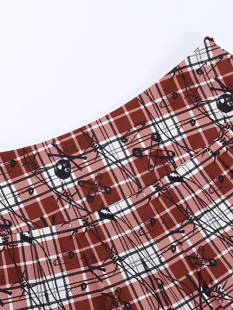 Close-up of the red plaid skirt waistband and top of the pleats, with black skull and safety-pin motifs across the tartan checks.
