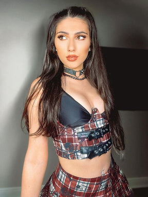 Angled indoor portrait of the red plaid underbust top and skirt set, showing the open bust, black buckle bands and lace-trimmed skirt.