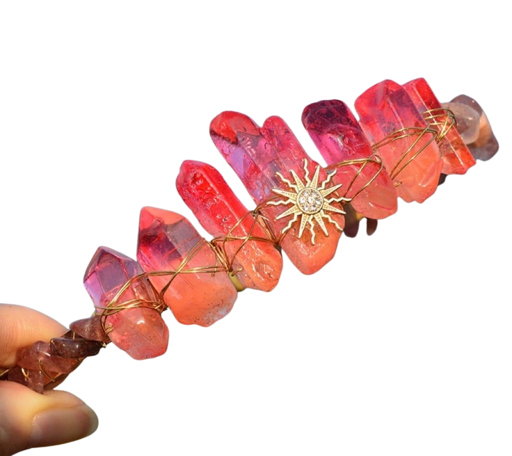 Red crystal point tiara on white with a gold-tone sun face at the centre and warm wire wrapping along the band.