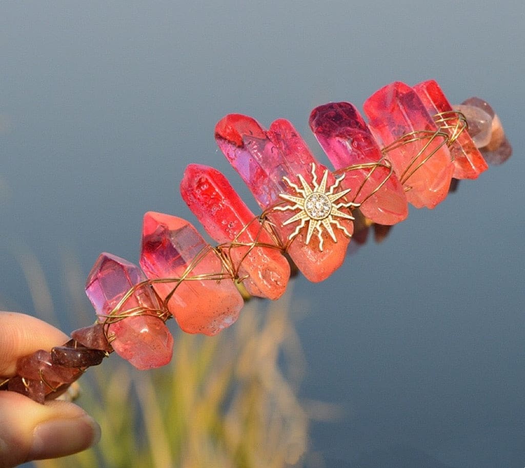 Red sun face tiara displayed outdoors, showing deep red points around the gold-tone face and radiating rays.