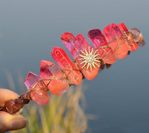 Red sun face tiara displayed outdoors, showing deep red points around the gold-tone face and radiating rays.