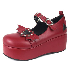 Red platform Mary Jane with a dark studded heart between red bat wings, a heart-shaped instep buckle and a matching red wedge sole.