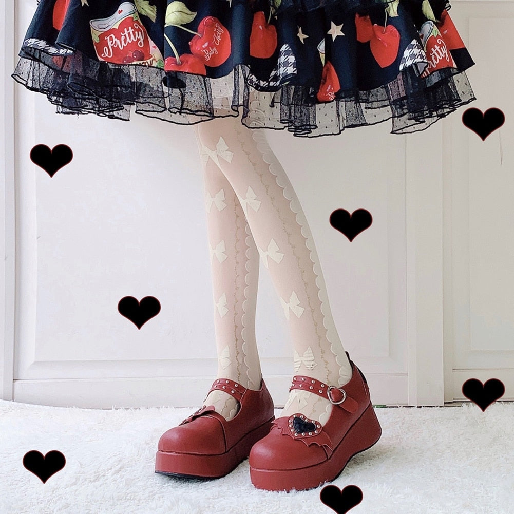 Red winged-heart Mary Janes worn with pale patterned stockings and a printed skirt, with black heart graphics around the outfit.