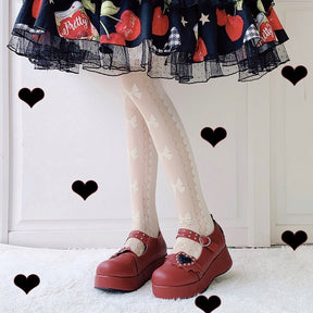 Red winged-heart Mary Janes worn with pale patterned stockings and a printed skirt, with black heart graphics around the outfit.