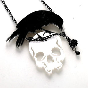 Angled close view of the crow-and-skull acrylic pendant, showing the reflective skull surface, chain accent and black rose detail.