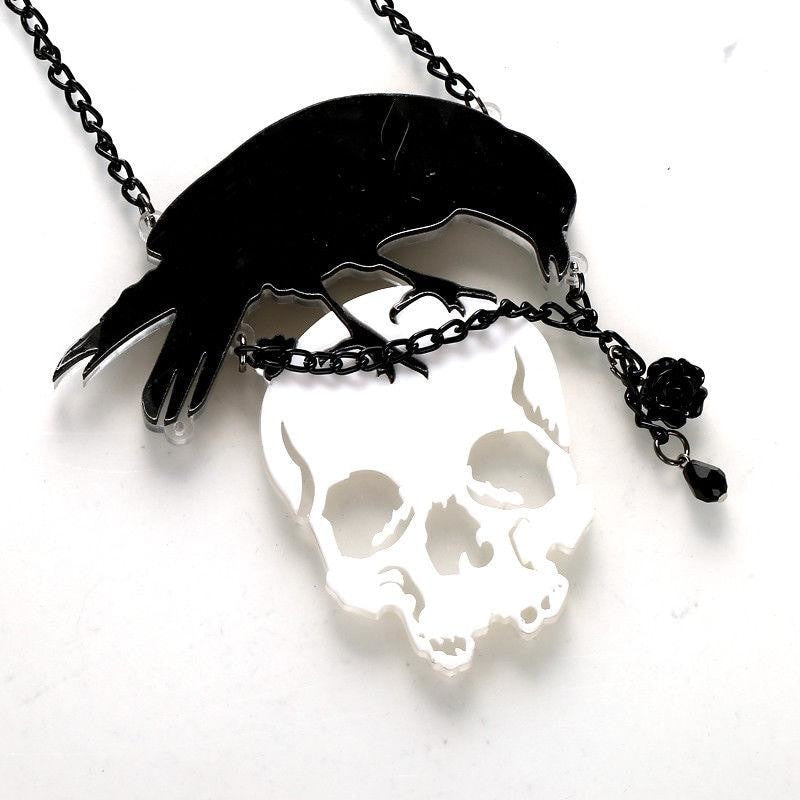 Angled close view of the crow-and-skull acrylic pendant, showing the reflective skull surface, chain accent and black rose detail.