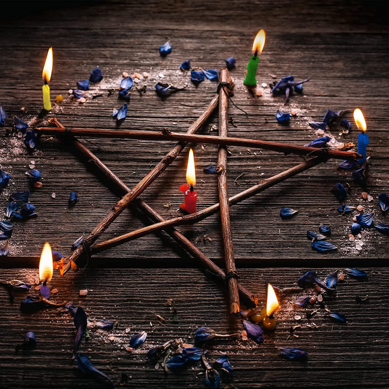 Lit candles arranged around a twig pentagram and blue crystals, illustrating a symbolic ritual display with separate props.
