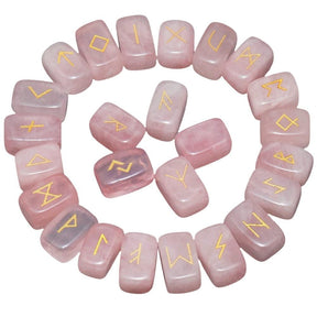 Rose quartz rune stones arranged in a circle, with pale pink polished surfaces and gold-coloured characters. The set includes a blank stone.