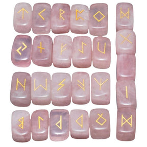 Rose quartz rune stone set laid out in rows, showing individual gold-coloured characters and one unmarked stone against pale pink surfaces.