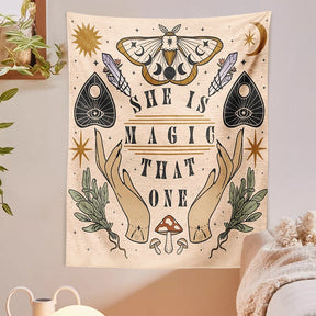 Moth and moon tapestry on a pale wall beside hanging greenery, with green botanical sprigs framing the central lettering.