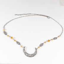 Silver-tone ornate crescent headdress with small amber-coloured beads and delicate ornamental links, arranged in an oval on a pale background with the clasp and chain visible.