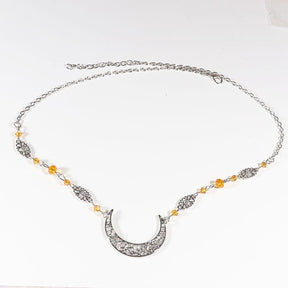 Silver-tone ornate crescent headdress with small amber-coloured beads and delicate ornamental links, arranged in an oval on a pale background with the clasp and chain visible.